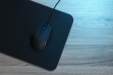 Photo of Computer mouse with mousepad on wooden table, top view. Space for text