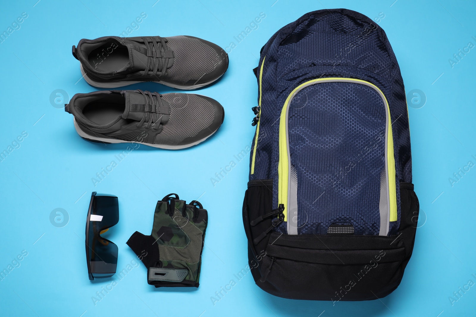 Photo of Backpack, sneakers, fingerless cycling glove and goggles on light blue background, flat lay