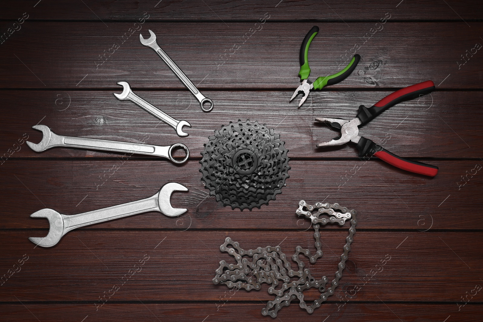 Photo of Wrenches, pliers, bicycle cassette and chain on wooden background, flat lay