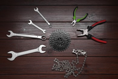 Wrenches, pliers, bicycle cassette and chain on wooden background, flat lay