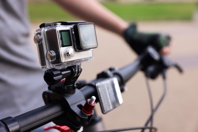 Photo of Man riding bicycle with modern action camera outdoors, closeup