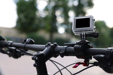 Photo of Modern action camera with mount on bicycle outdoors, closeup