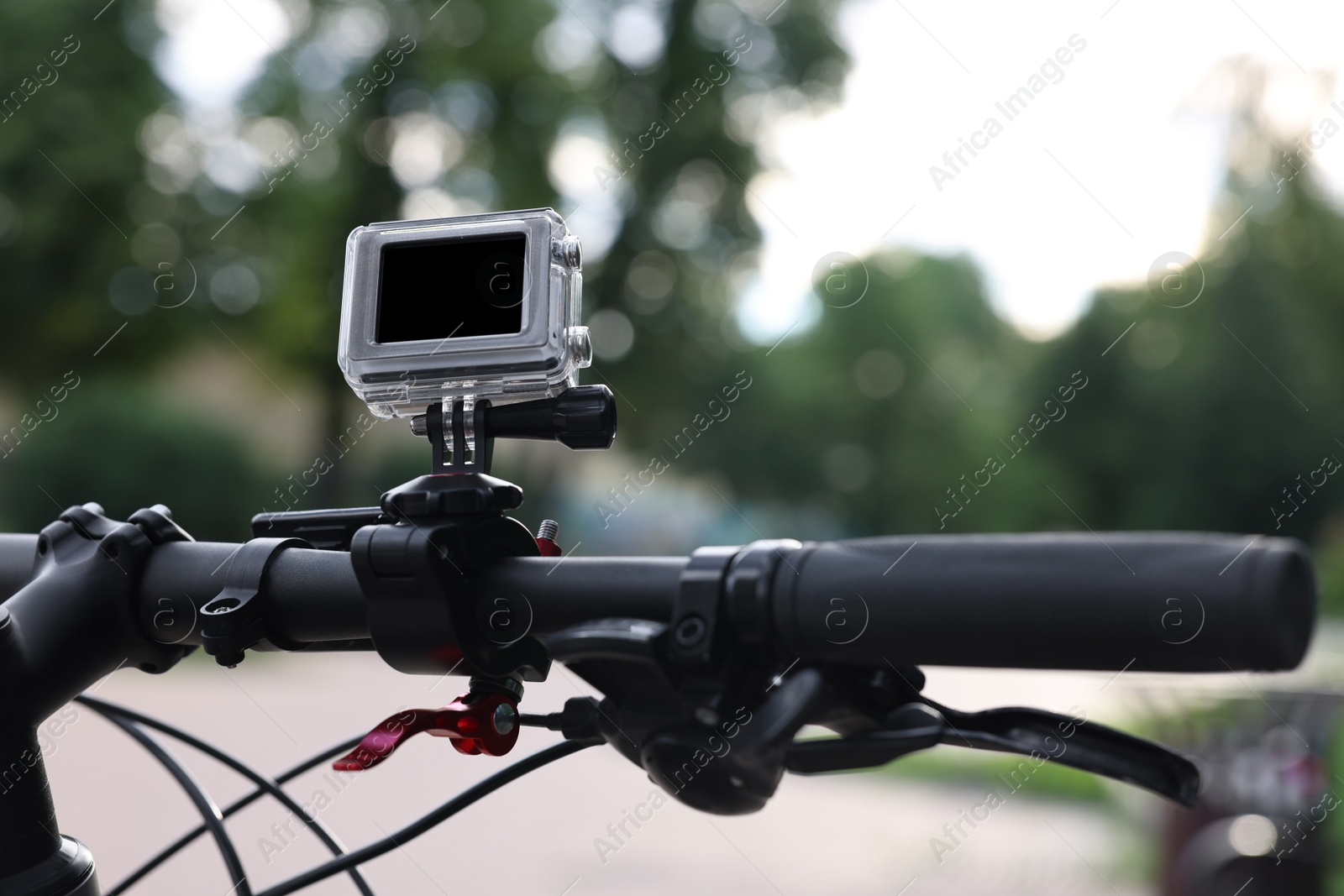 Photo of Modern action camera with mount on bicycle outdoors, closeup