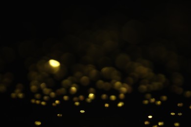 Photo of Beautiful shiny golden glitter on black background, closeup