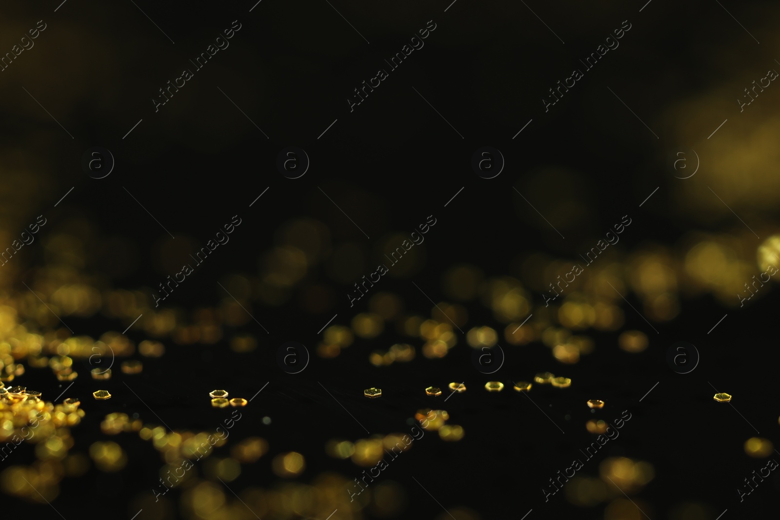 Photo of Beautiful shiny golden glitter on black background, closeup