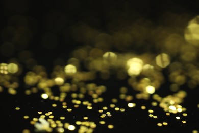 Photo of Beautiful shiny golden glitter on black background, closeup