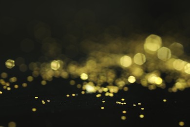 Photo of Beautiful shiny golden glitter on black background, closeup