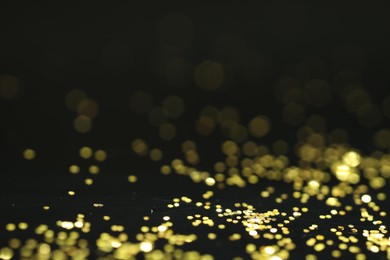 Photo of Beautiful shiny golden glitter on black background, closeup