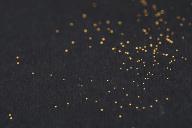 Photo of Beautiful shiny golden glitter on black background, closeup