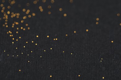 Photo of Beautiful shiny golden glitter on black background, closeup