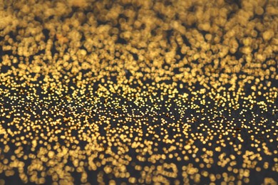 Photo of Beautiful shiny golden glitter on black background, closeup