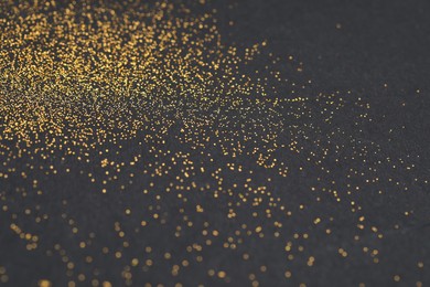 Photo of Beautiful shiny golden glitter on black background, closeup