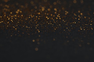 Photo of Beautiful shiny golden glitter on black background, closeup