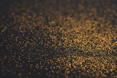 Photo of Beautiful shiny golden glitter on black background, closeup