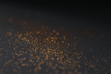 Photo of Beautiful shiny golden glitter on black background, closeup