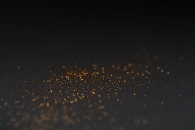 Photo of Beautiful shiny golden glitter on black background, closeup