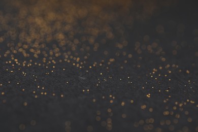 Photo of Beautiful shiny golden glitter on black background, closeup