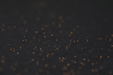 Photo of Beautiful shiny golden glitter on black background, closeup