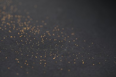 Photo of Beautiful shiny golden glitter on black background, closeup