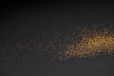 Photo of Beautiful shiny golden glitter on black background, closeup