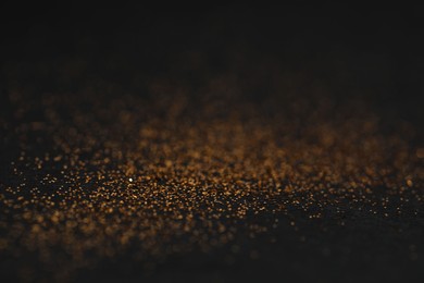 Photo of Beautiful shiny golden glitter on black background, closeup