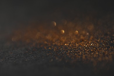 Photo of Beautiful shiny golden glitter on black background, closeup