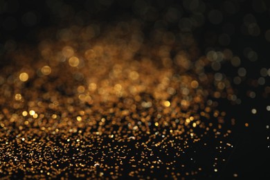 Photo of Beautiful shiny golden glitter on black background, closeup