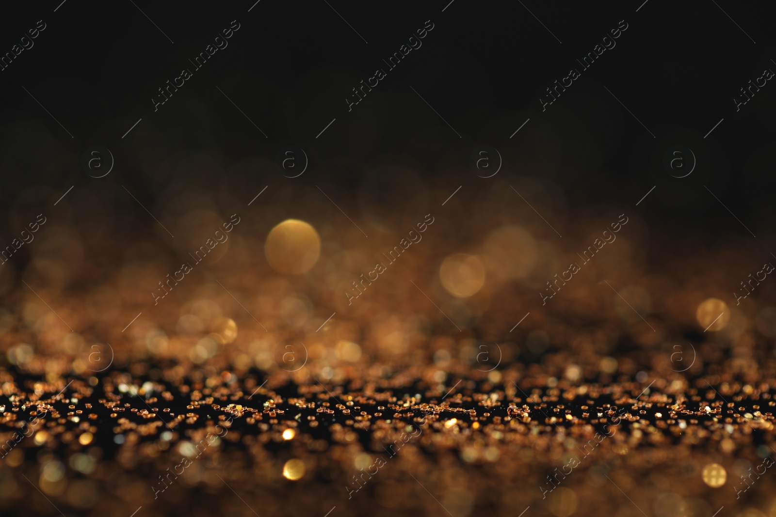 Photo of Beautiful shiny golden glitter on black background, closeup