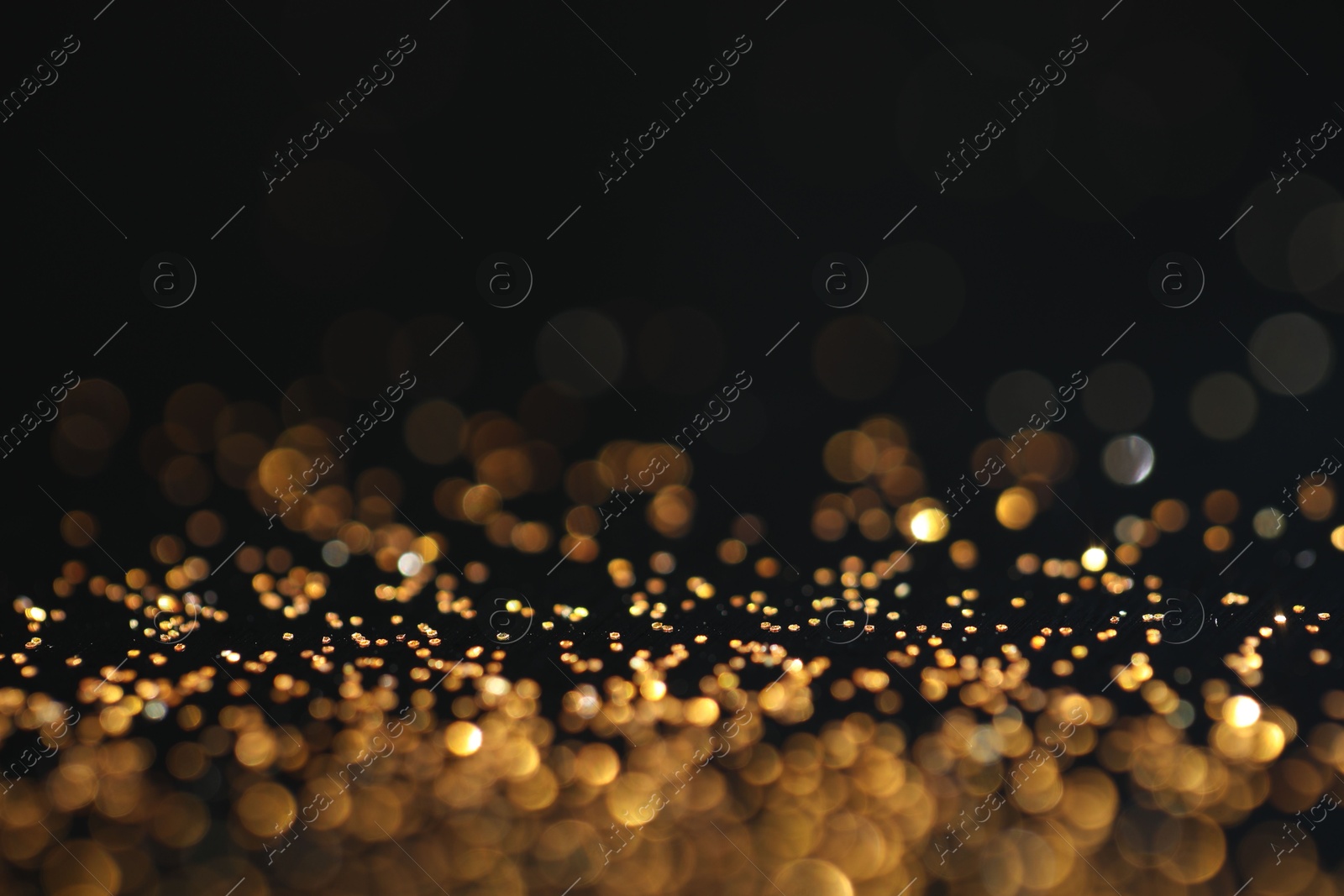 Photo of Beautiful shiny golden glitter on black background, closeup