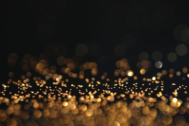 Photo of Beautiful shiny golden glitter on black background, closeup