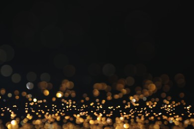 Photo of Beautiful shiny golden glitter on black background, closeup