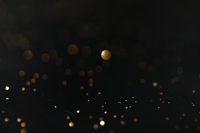 Photo of Beautiful shiny golden glitter on black background, closeup