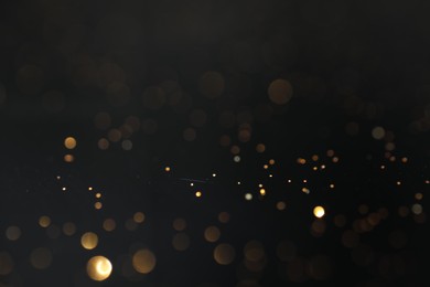 Photo of Beautiful shiny golden glitter on black background, closeup