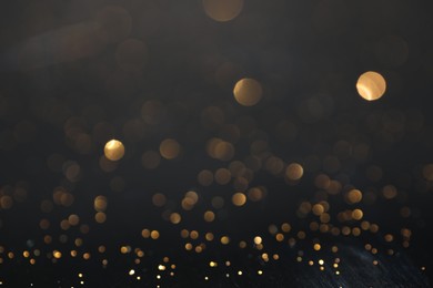 Photo of Beautiful shiny golden glitter on black background, closeup