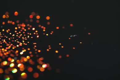 Photo of Beautiful shiny golden glitter on black background, closeup