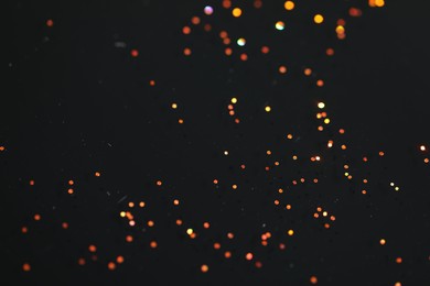 Photo of Beautiful shiny golden glitter on black background, closeup