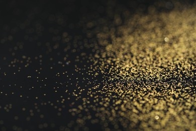 Photo of Beautiful shiny golden glitter on black background, closeup