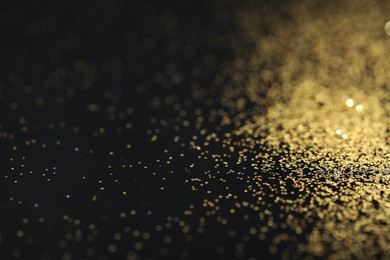 Photo of Beautiful shiny golden glitter on black background, closeup