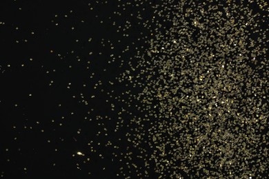 Photo of Beautiful shiny golden glitter on black background, top view