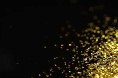 Photo of Beautiful shiny golden glitter on black background, closeup