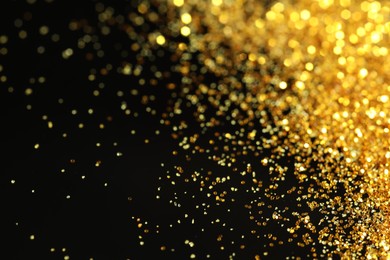 Photo of Beautiful shiny golden glitter on black background, closeup