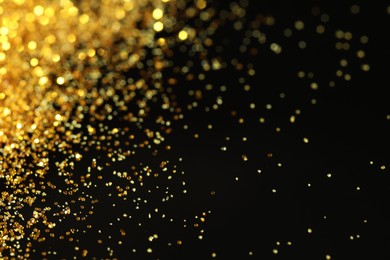 Photo of Beautiful shiny golden glitter on black background, closeup