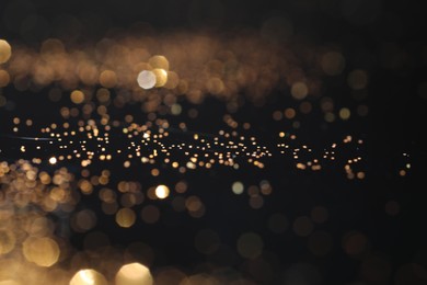 Photo of Beautiful shiny golden glitter on black background, closeup