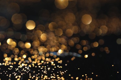 Photo of Beautiful shiny golden glitter on black background, closeup