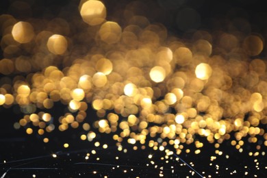 Photo of Beautiful shiny golden glitter on black background, closeup