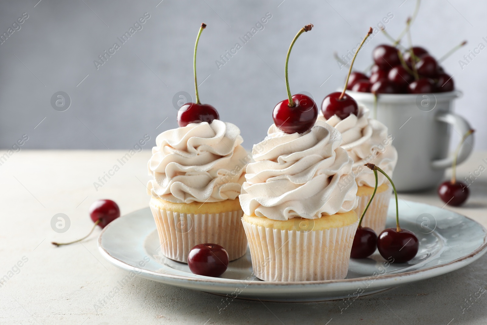 Photo of Delicious cupcakes with cream and cherries on light textured table, closeup