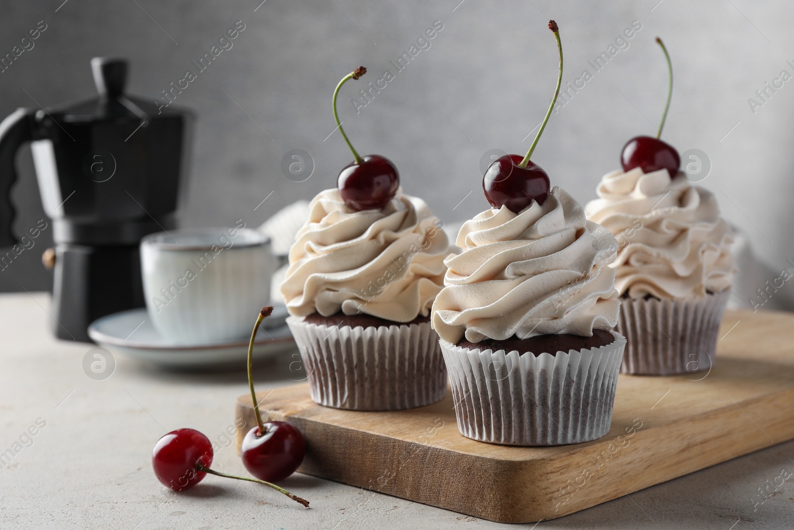 Photo of Delicious cupcakes with cream and cherries on light textured table, closeup