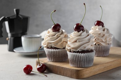 Photo of Delicious cupcakes with cream and cherries on light textured table, closeup