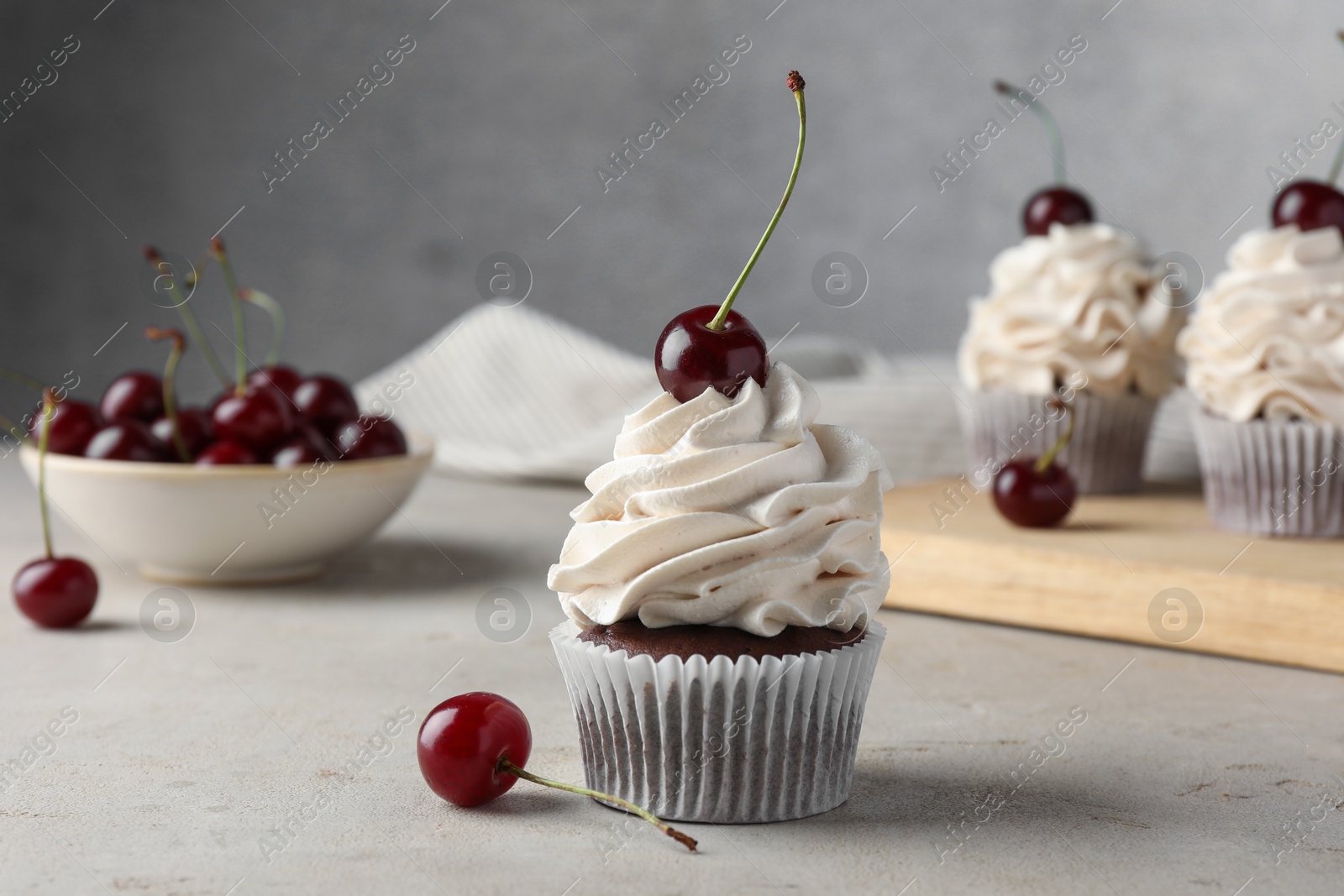 Photo of Delicious cupcakes with cream and cherries on light textured table