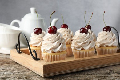 Photo of Delicious cupcakes with cream and cherries on wooden table, closeup